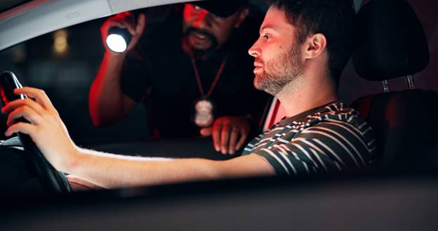 A man is being questioned by a police officer at night, the officer holding a flashlight. The image relates to topics of illegal search and seizure.